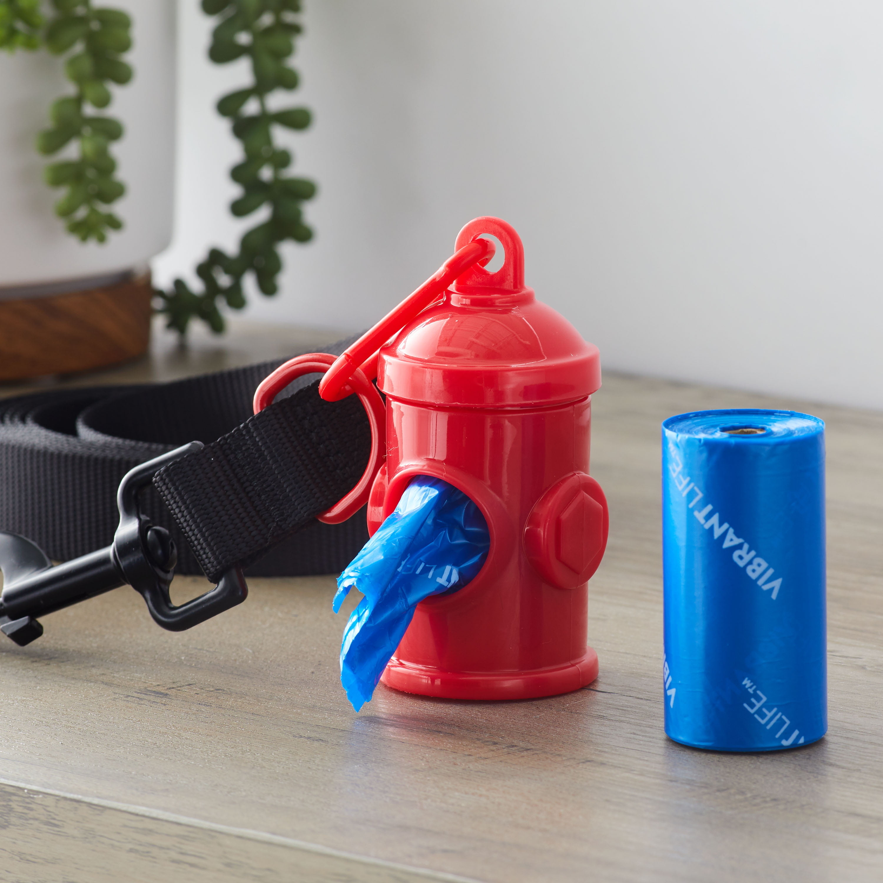 Red dog waste bag dispenser attached to a leash with a blue bag roll next to it. Perfect for pet owners on the go