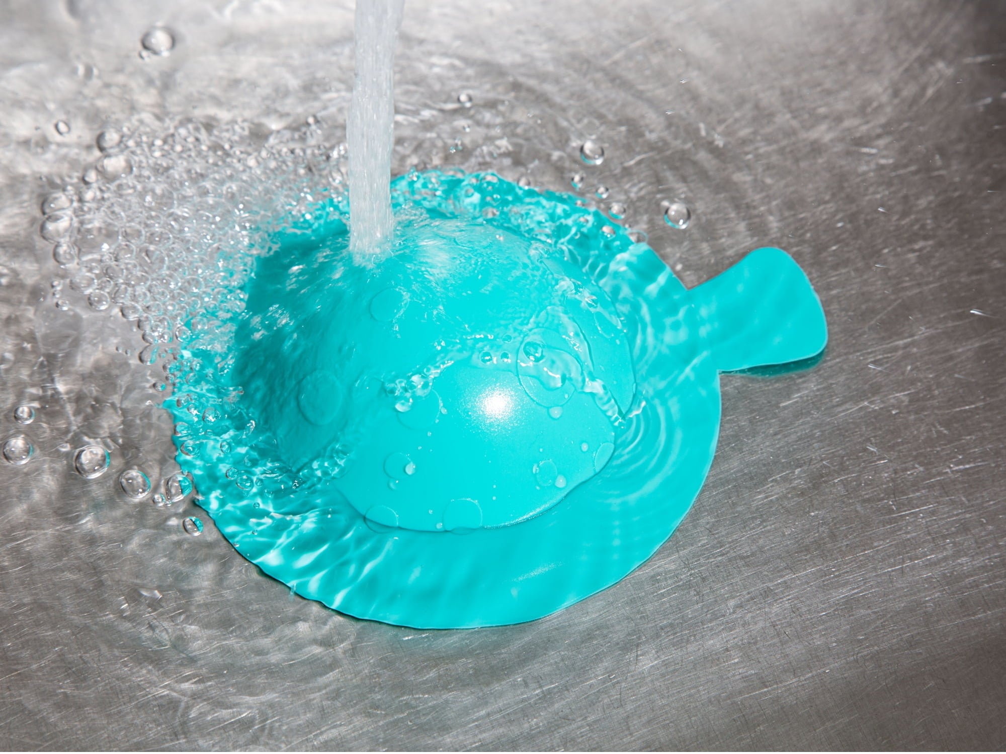 Water pouring into a teal plastic neti pot, an item used for nasal irrigation