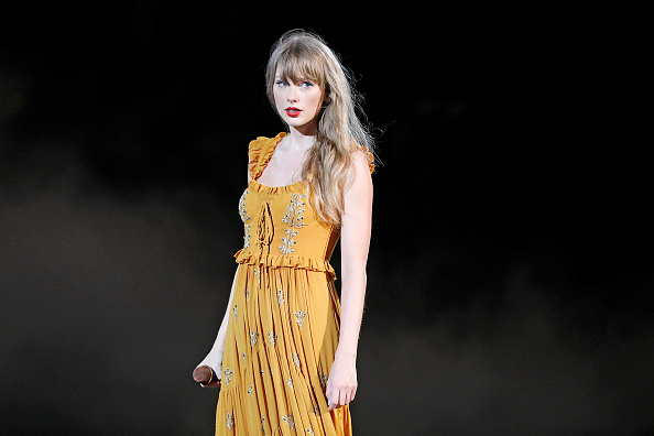Taylor Swift wearing a sleeveless, embellished yellow dress on stage