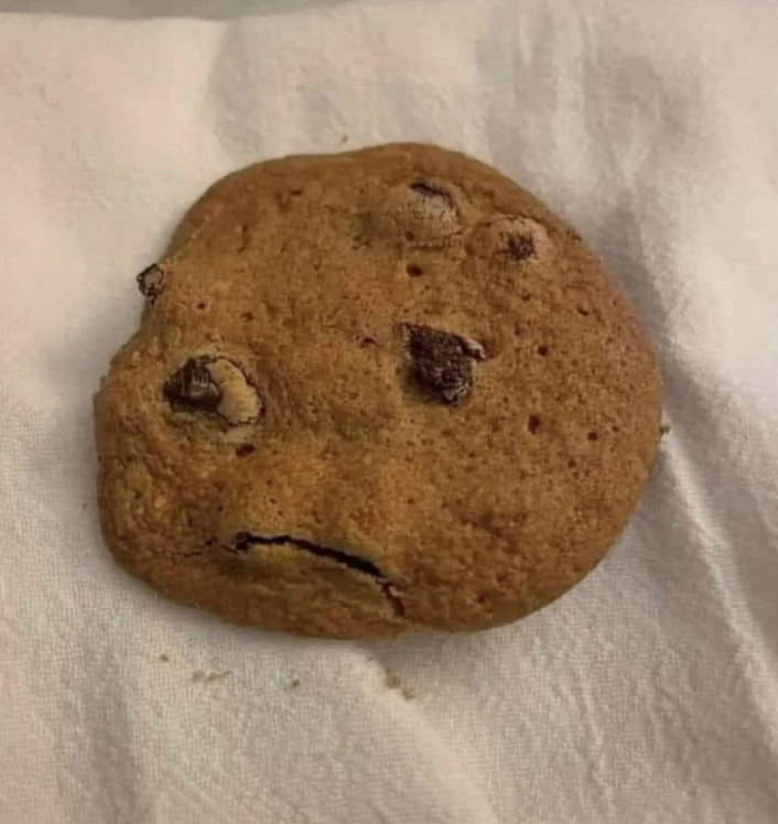 A chocolate chip cookie with a pattern that resembles a frowning face