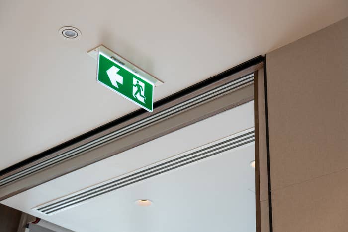 Emergency exit sign with leftward arrow hanging from a ceiling beside a doorway