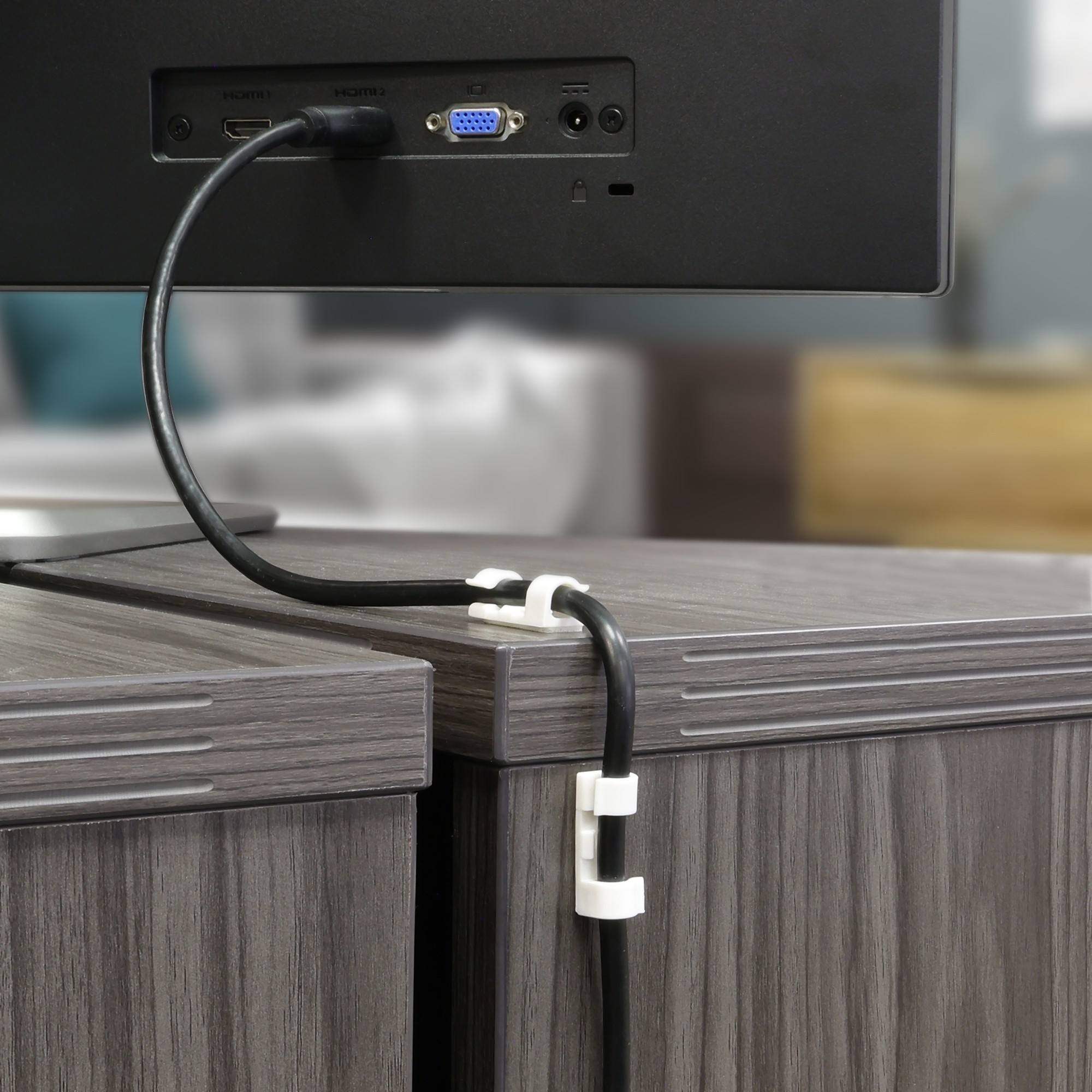 Cable management clip on a desk organizing wires, with a TV in the background