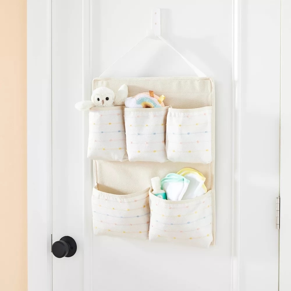 Hanging fabric storage with multiple pockets filled with baby items on a door