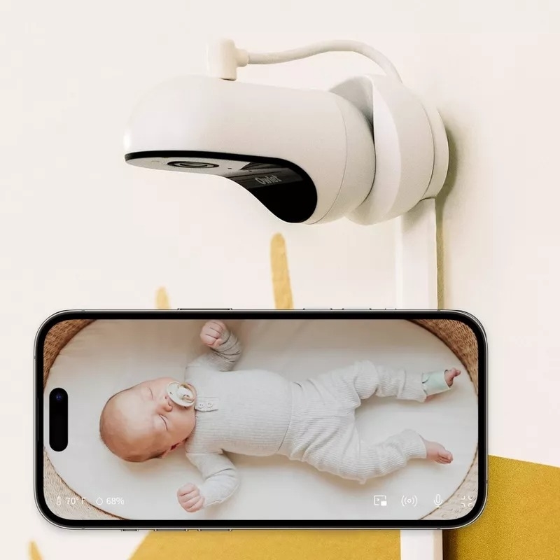 Baby monitor camera above a smartphone showing live feed of a sleeping baby in a onesie