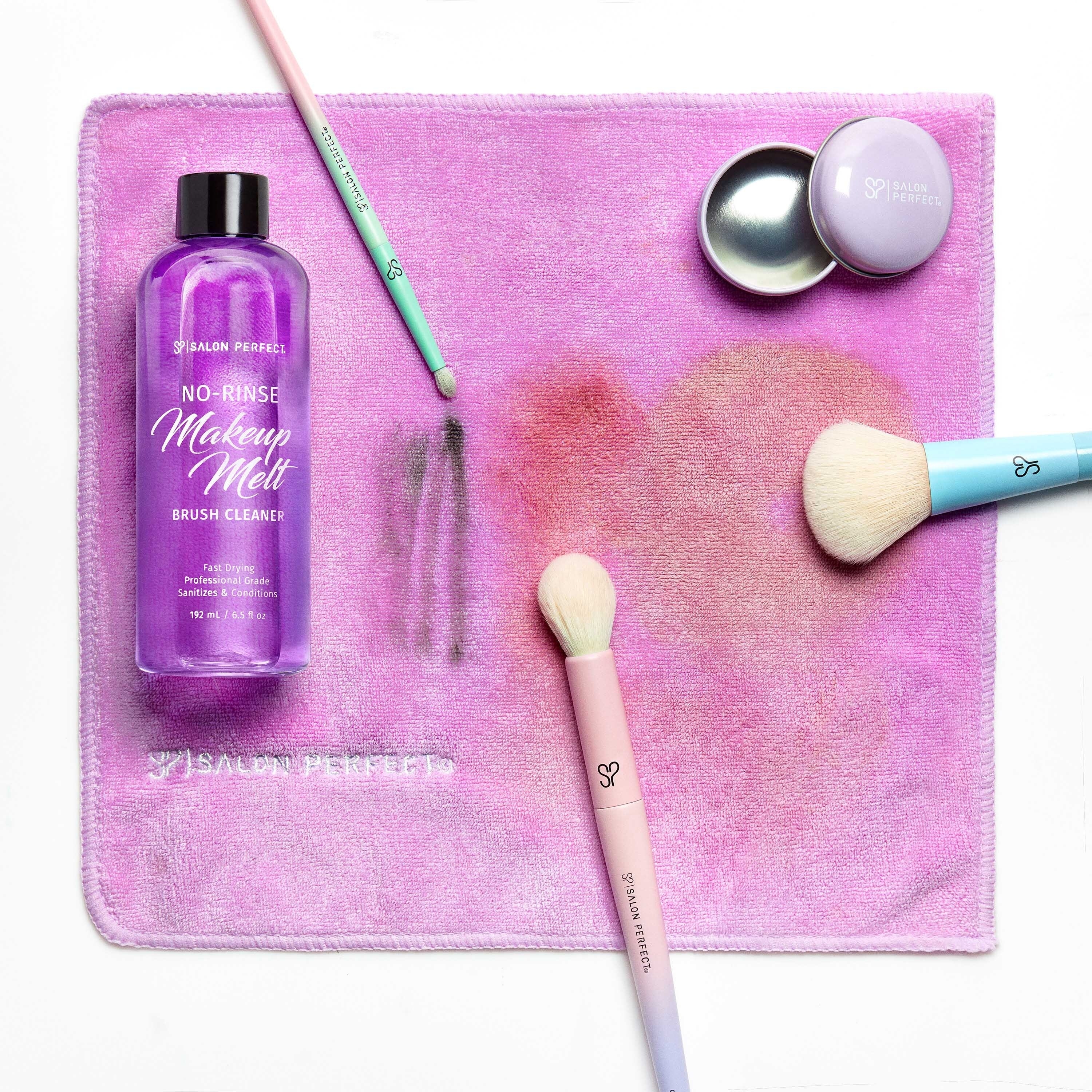 Makeup brush cleaner bottle, two brushes, and a sponge on a mat with a smudge mark
