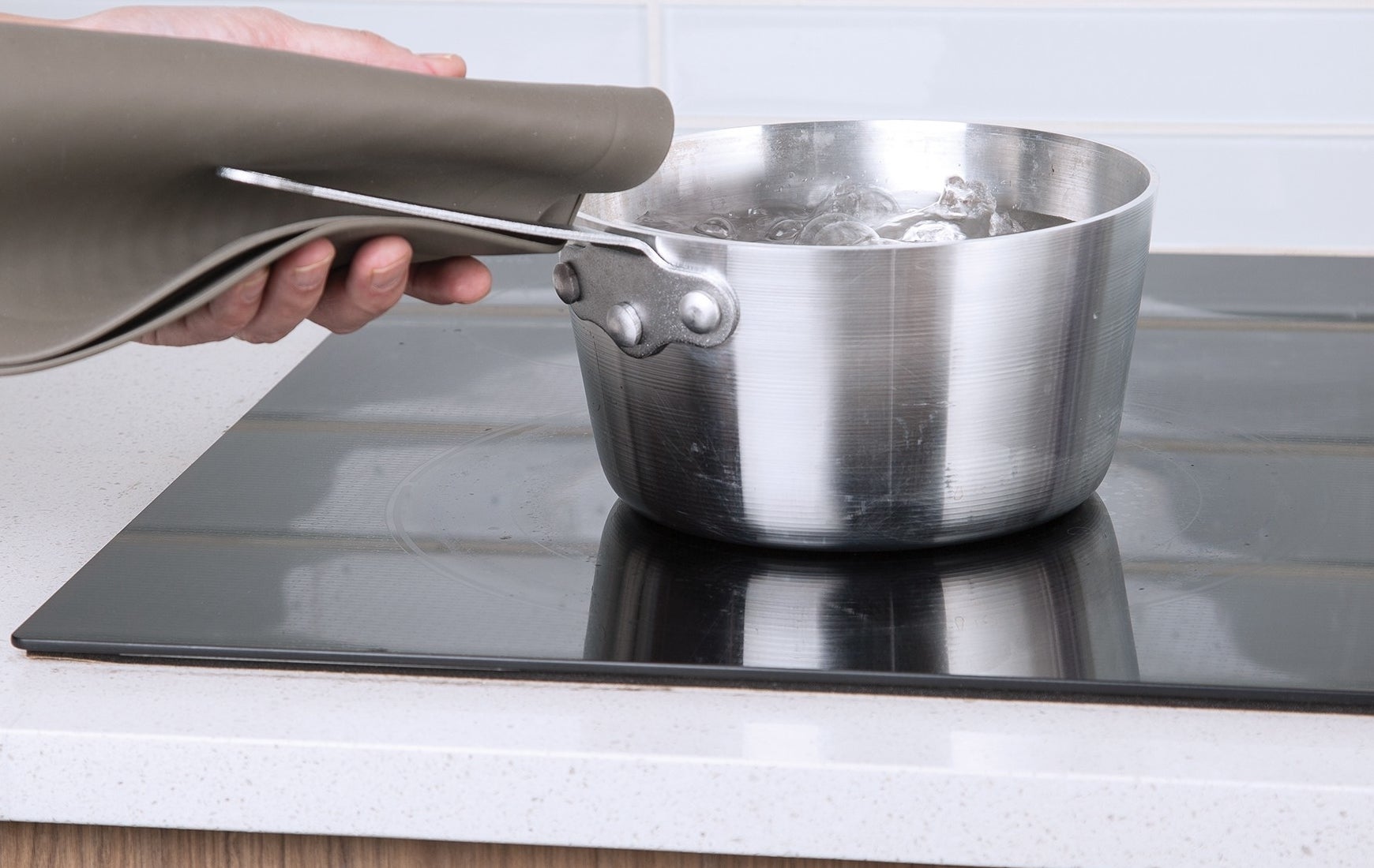 Person using the mat as a potholder to hold a pot handle on a stove