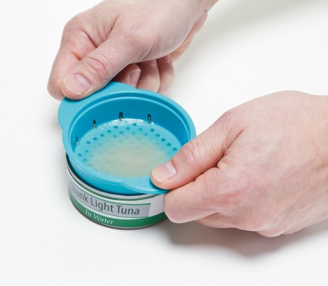 Person&#x27;s hands using a can strainer on a tuna can