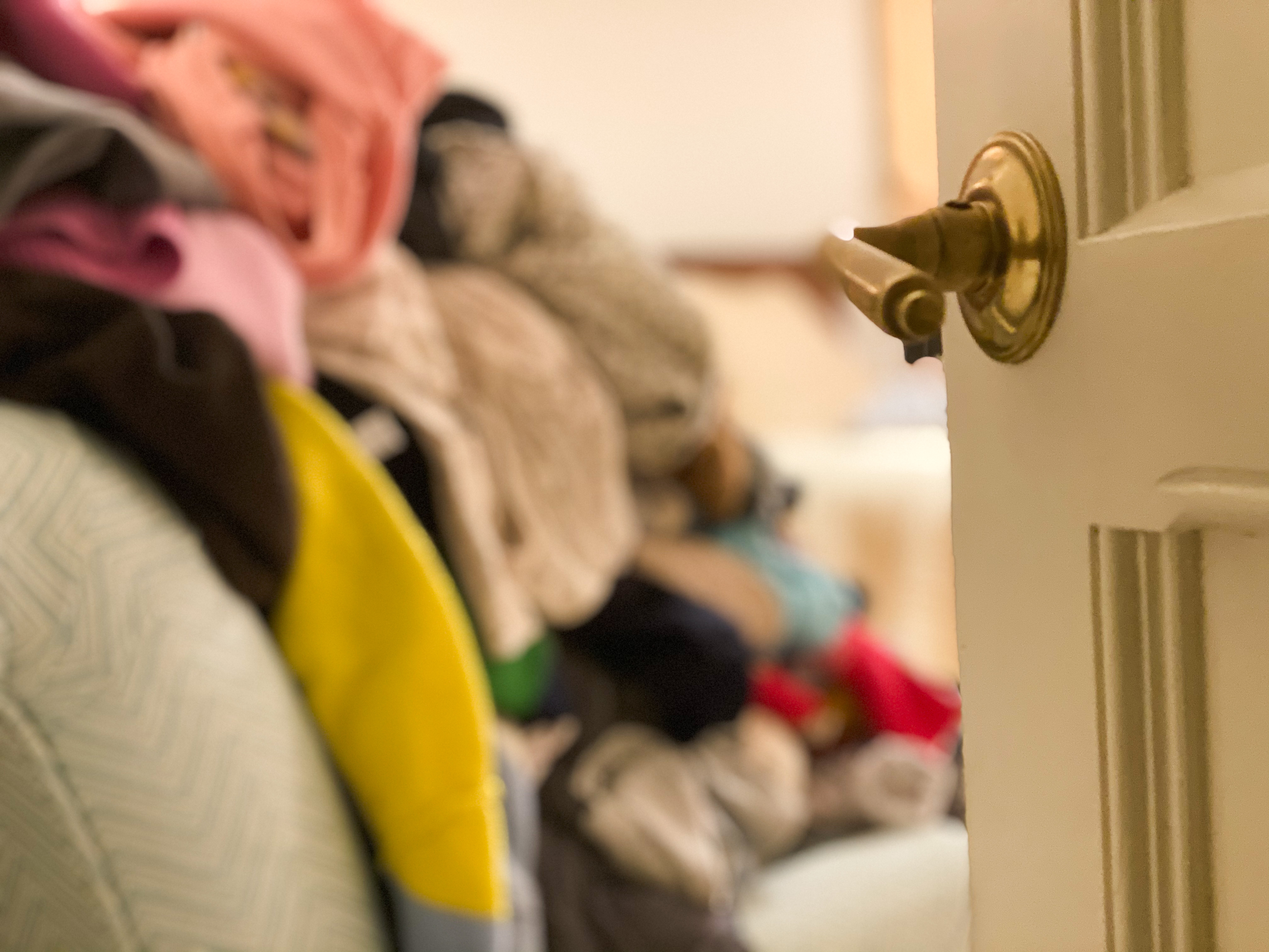 Pile of unfolded clothes on a couch viewed from behind a slightly open door