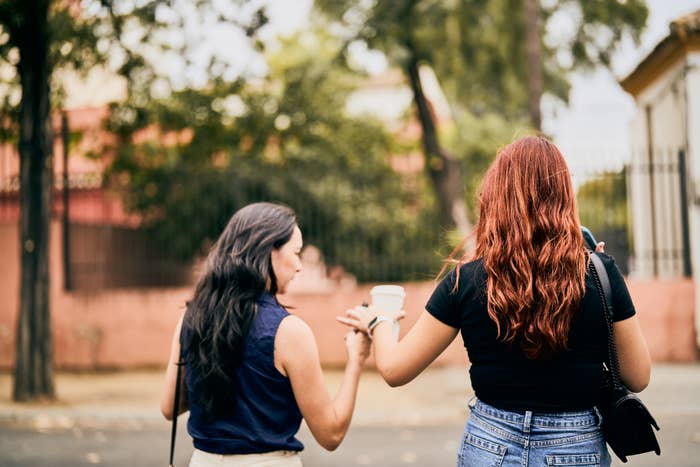 Two people facing away, one holding a smartphone, casual attire, standing outdoors