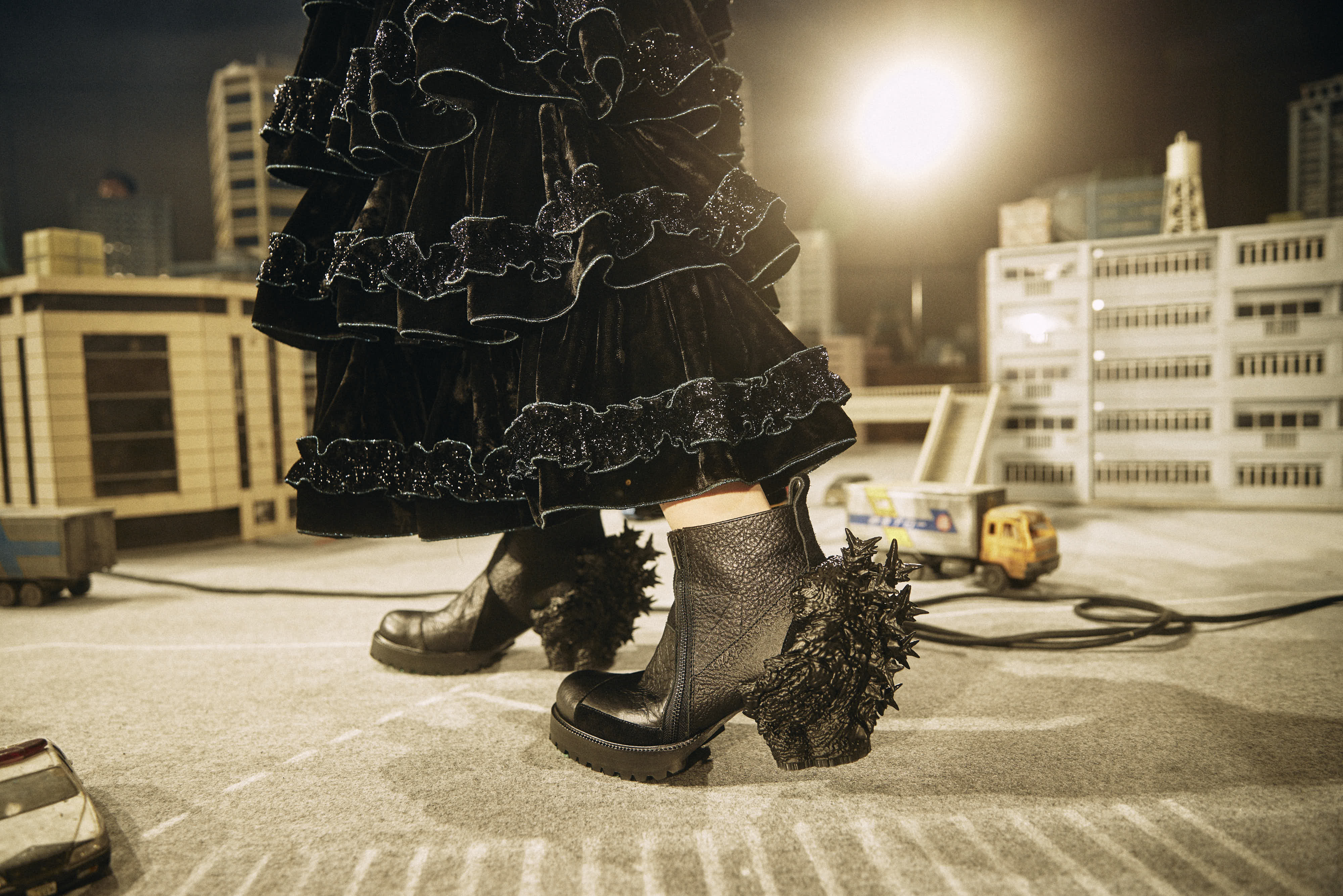 黒いレースのドレスとブーツを履いた人物が、屋上で夜景を背にポーズをとっています。