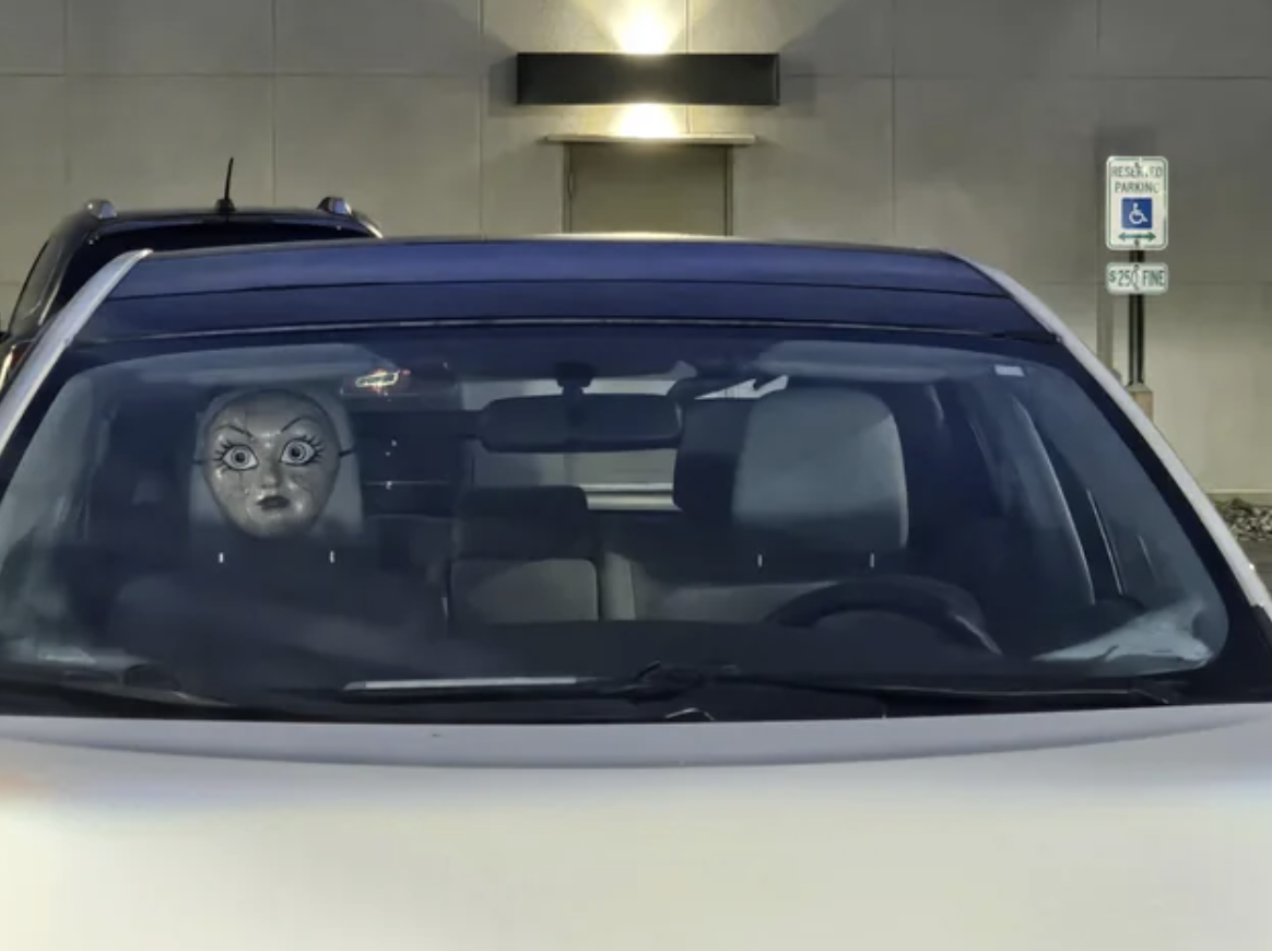 Car windscreen with a realistic face mask on the headrest creating an illusion of a passenger