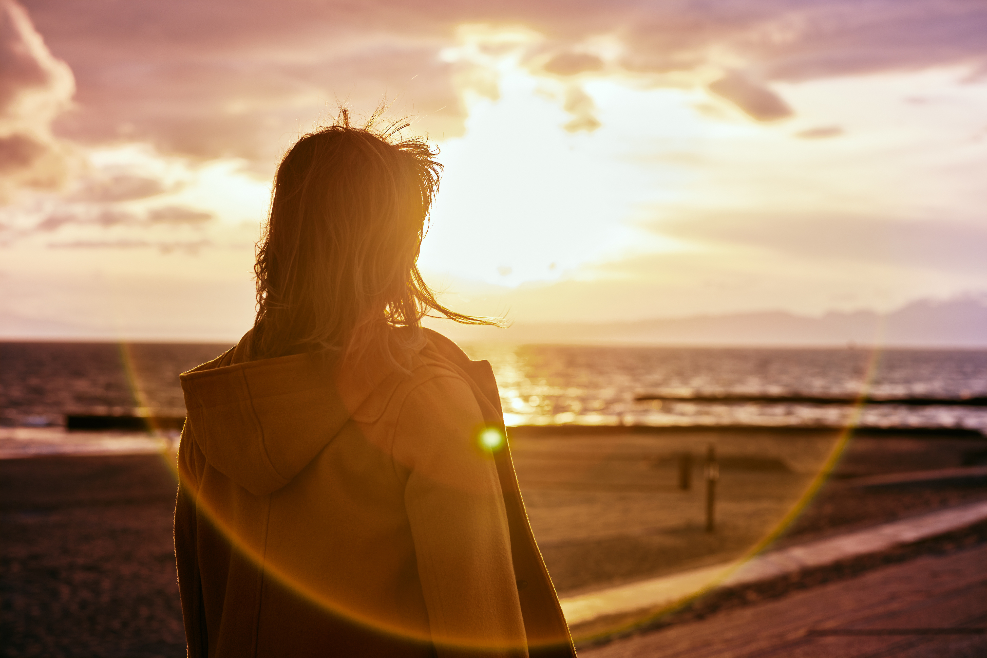 Person facing sunset on beach, evoking a sense of contemplation or tranquility