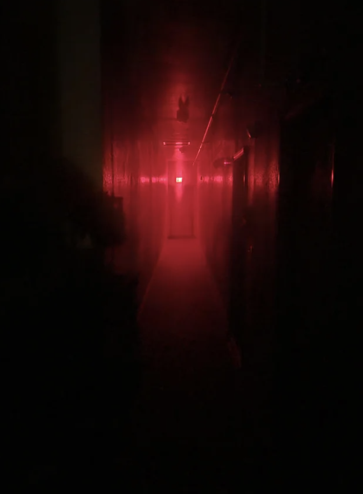 Dimly lit hallway with a red light near an exit sign
