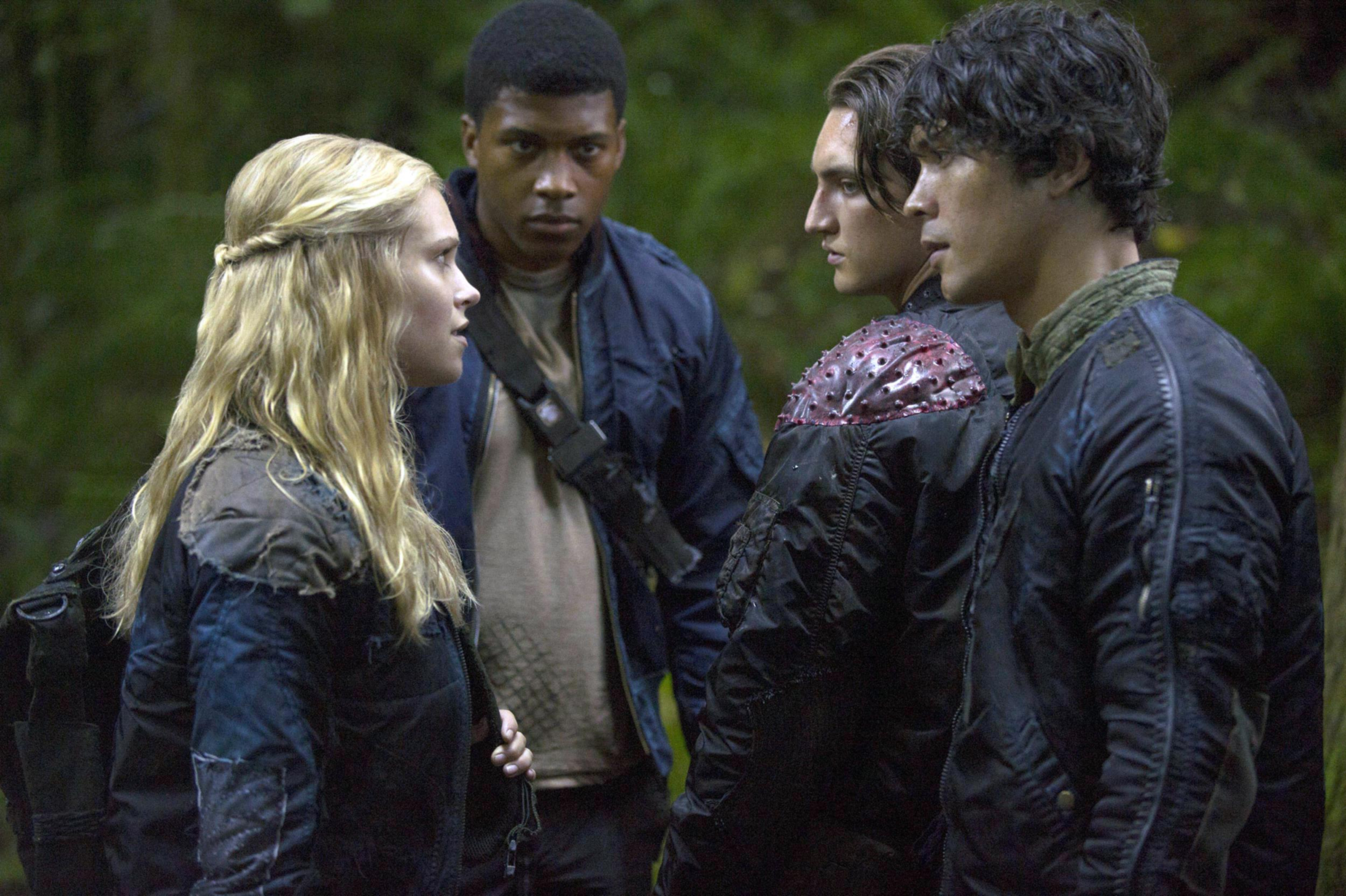 Group of characters from a TV show in a tense discussion in a forest setting