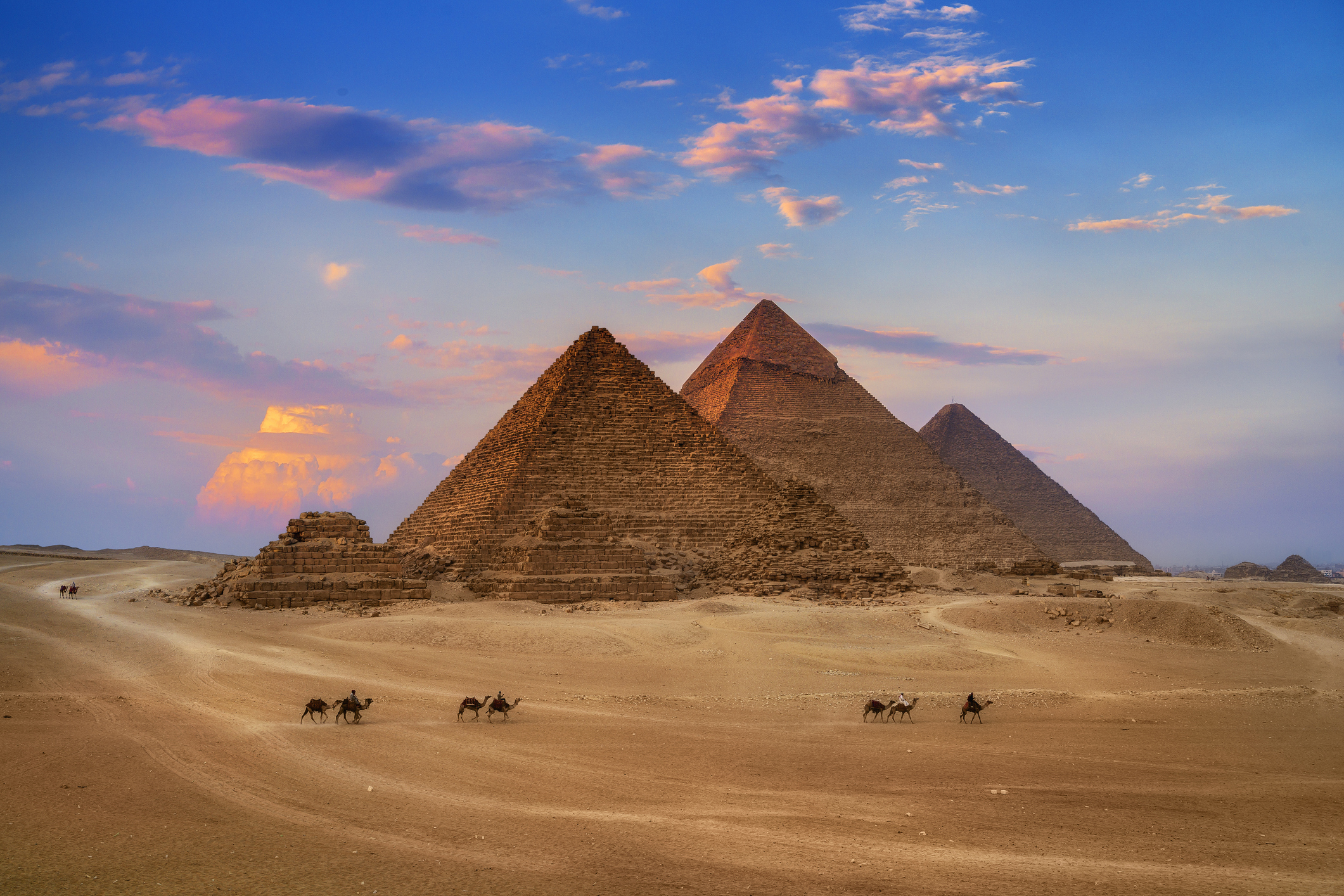 Three pyramids in Egypt with people on camels in the foreground