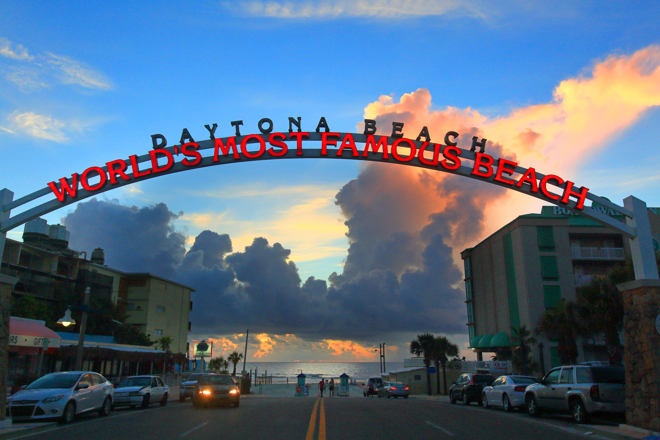 Sunset at Daytona Beach with iconic arch reading &quot;WORLD&#x27;S MOST FAMOUS BEACH&quot; over a street leading to the ocean