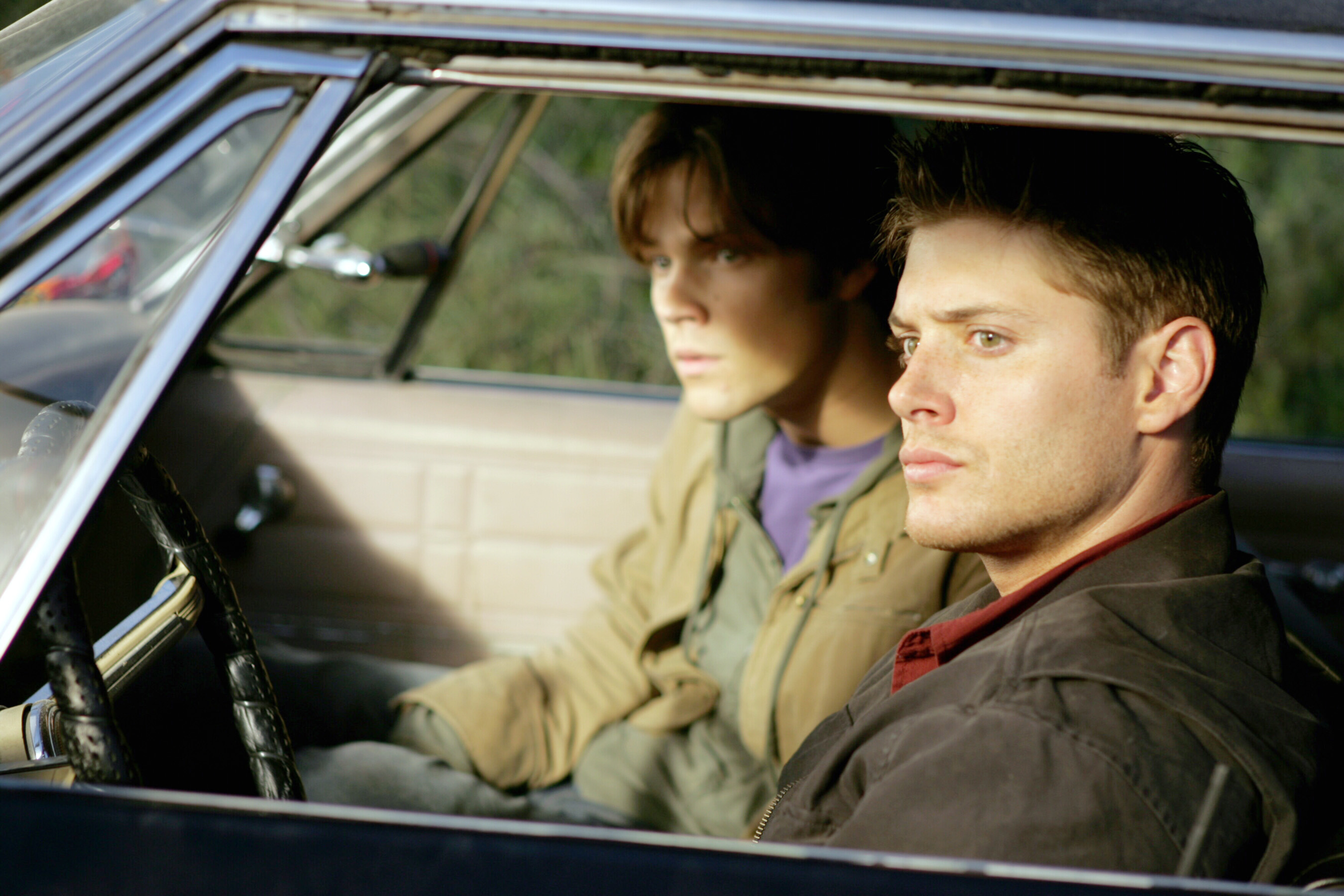 Two actors portraying Sam and Dean Winchester sitting in a car, looking intently in the same direction