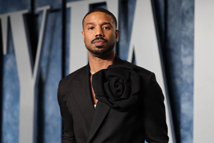 Michael B. Jordan in a suit with a large floral adornment on the lapel, posing at an event