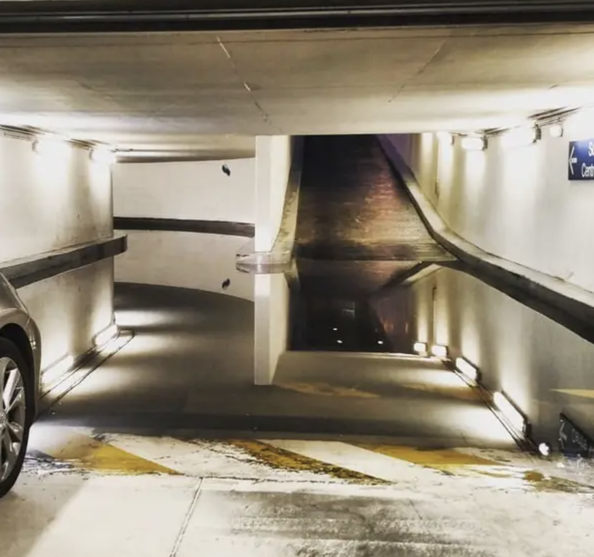 An empty parking garage ramp with lighting along the path and a car partially visible