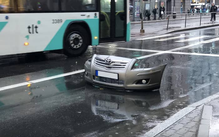Detached car front bumper in street with oncoming bus