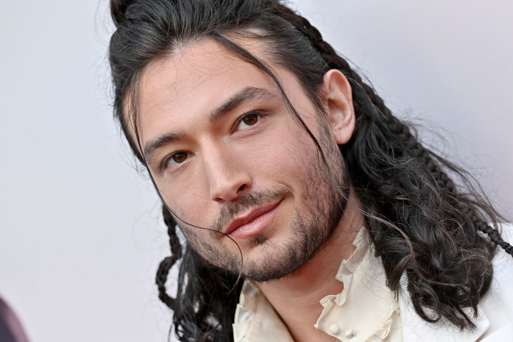 Ezra with a braided hairstyle, wearing a ruffled shirt, looking at the camera