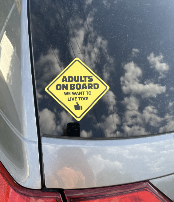 Sticker on a car window reads &quot;ADULTS ON BOARD, WE WANT TO LIVE TOO!&quot;, parody of baby on board signs