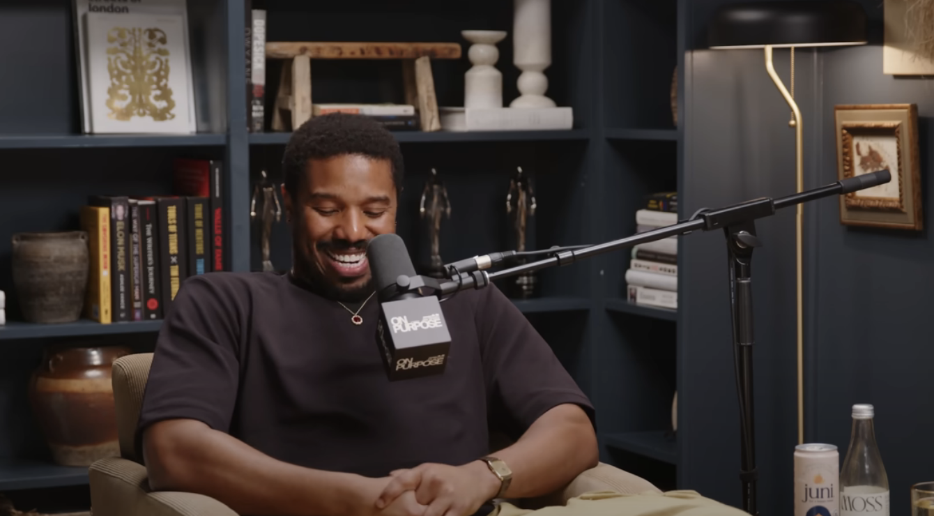Michael laughing while sitting at a podcast setup with microphone and headphones