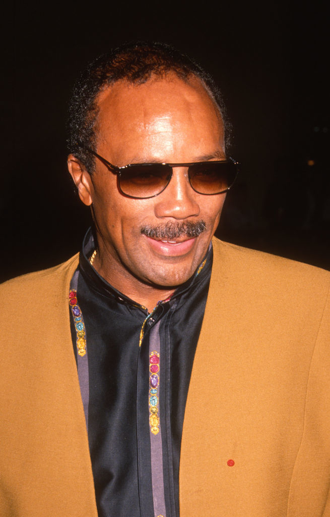 Quincy wearing sunglasses and a camel-colored jacket with decorative buttons