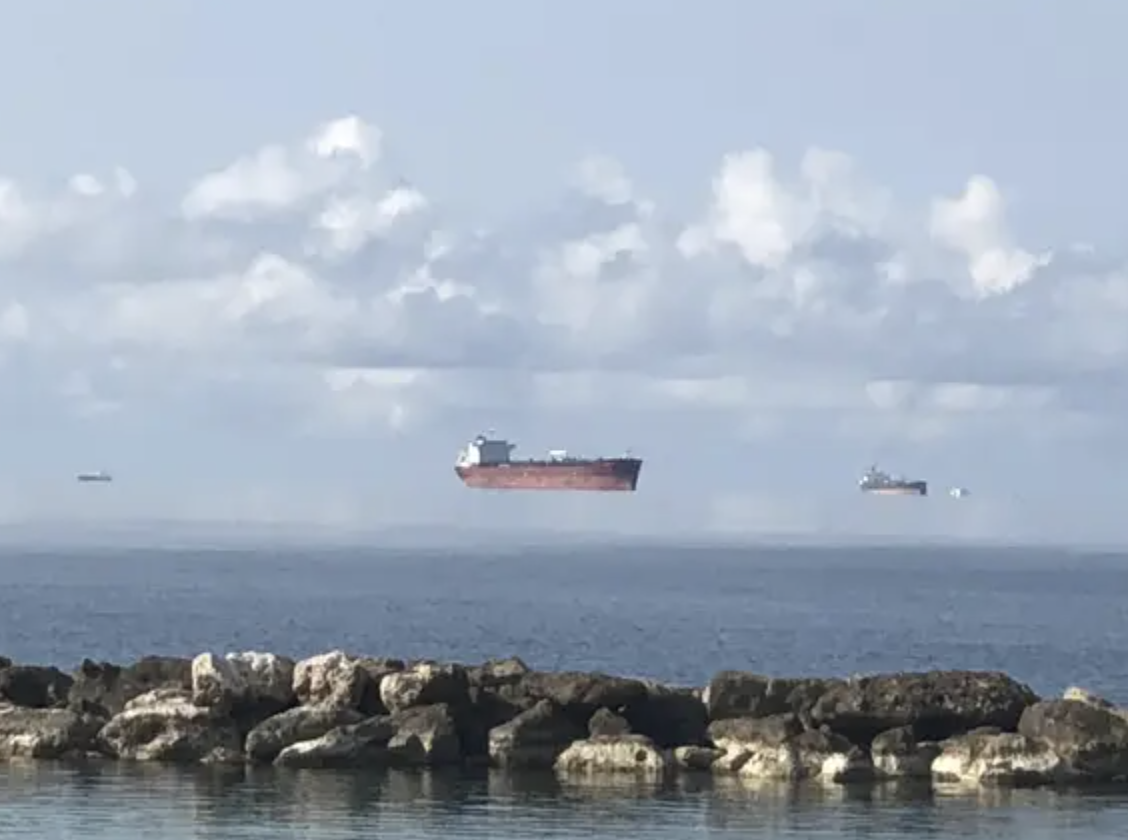 Ship appears to float above the ocean due to an optical illusion with clear skies