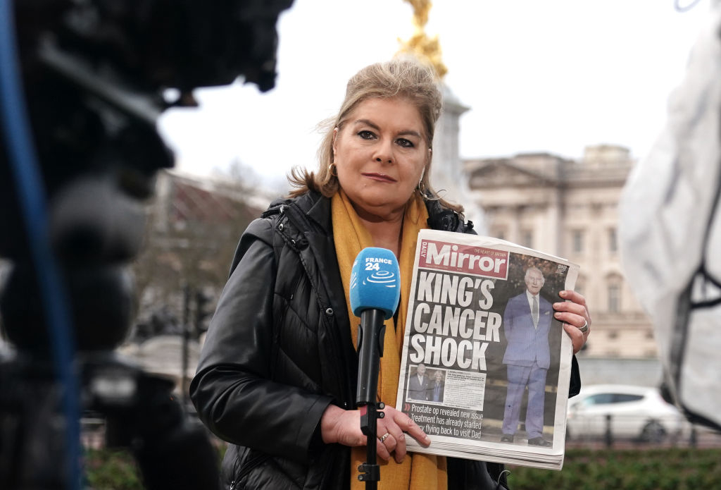 Reporter on location holding up a &quot;Mirror&quot; newspaper with a headline about a king&#x27;s health
