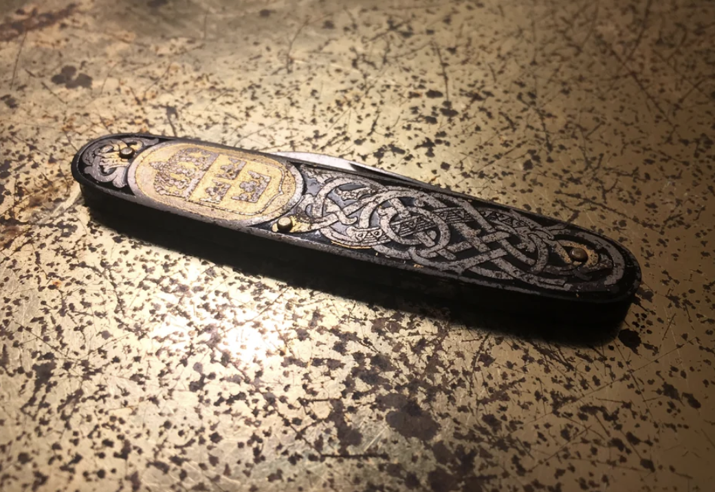 Decorative, vintage pocket knife with intricate designs, placed on a textured surface
