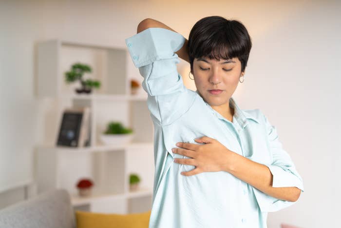 Person stretching in a light shirt, doing a breast exam