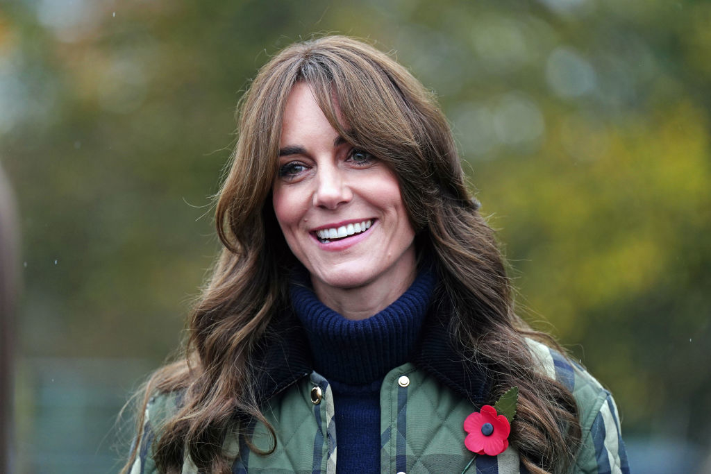 Kate with a poppy pin smiling outdoors, wearing a dark turtleneck and a camo-patterned jacket