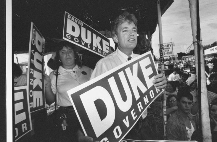 Person at a political rally holding a &quot;DUKE for GOVERNOR&quot; sign with supporters in the background