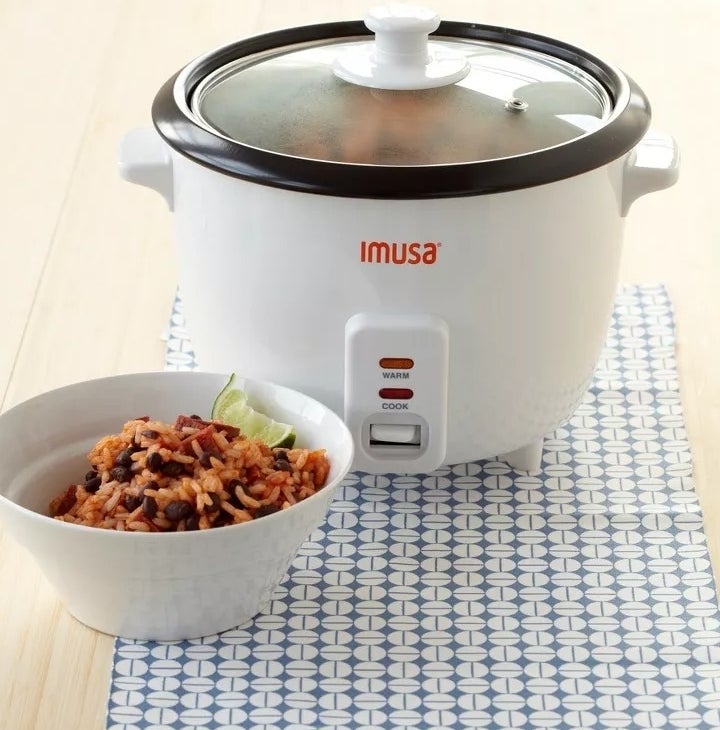The mini rice cooker, on a counter, next to a bowl of cooked rice and beans