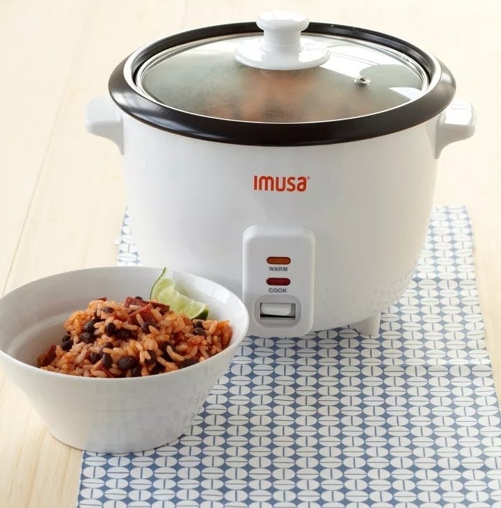 The mini rice cooker, on a counter, next to a bowl of cooked rice and beans