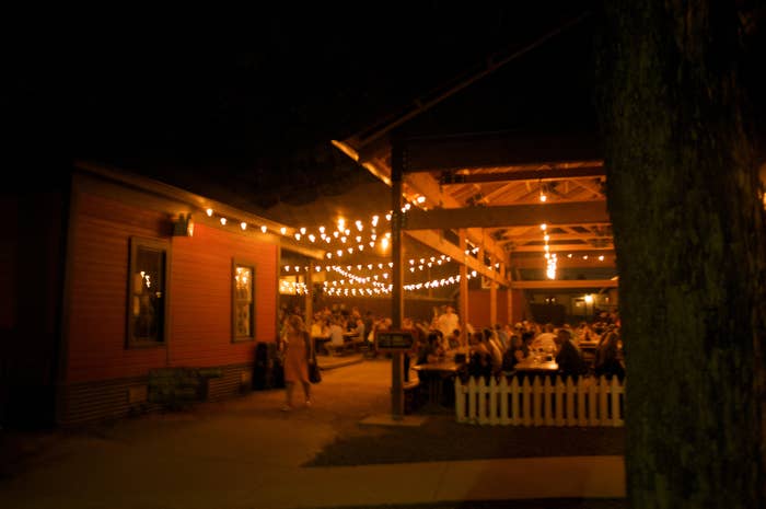 Outdoor evening scene at a dining area with string lights and patrons at tables