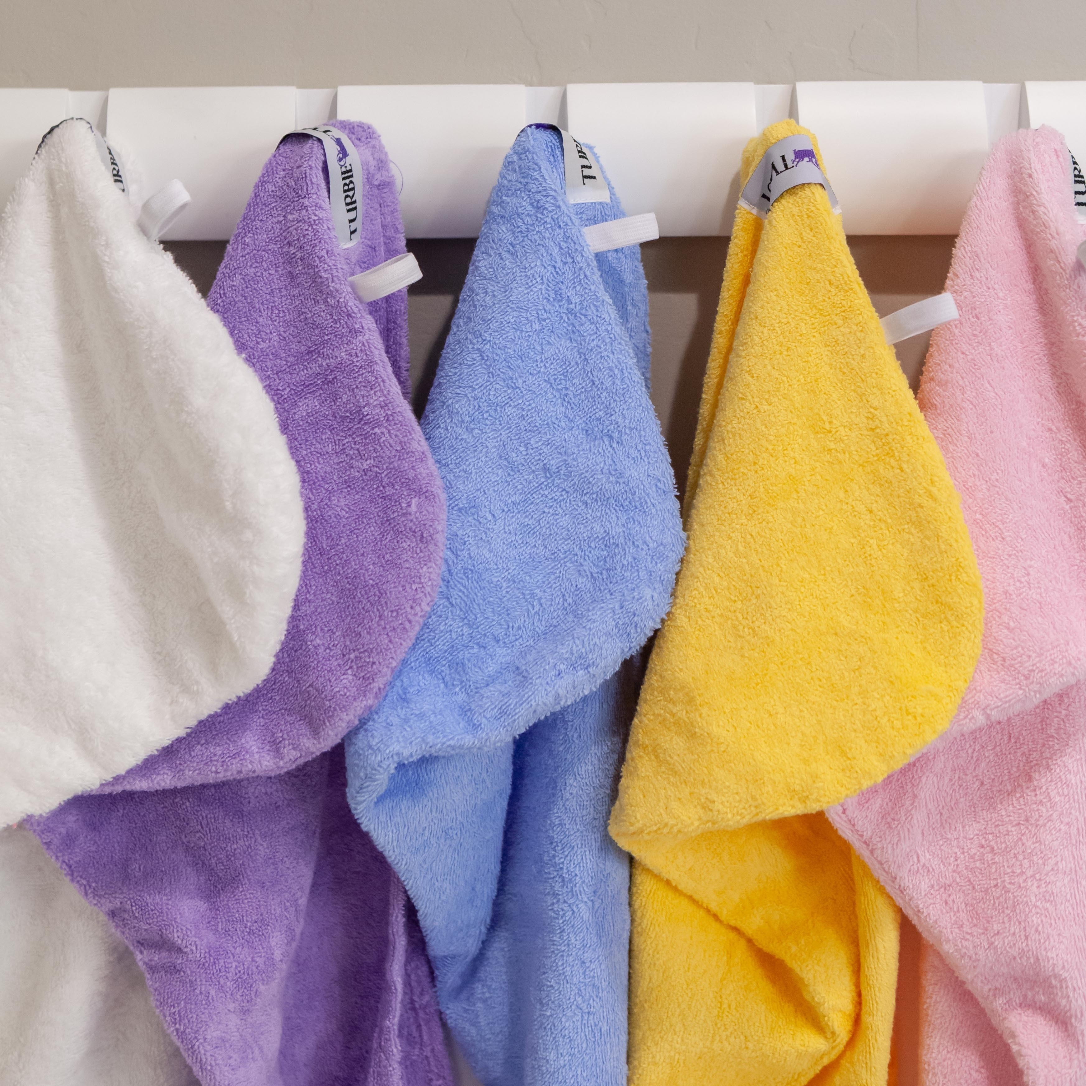 The towels hanging for display in white, purple, blue, yellow and pink
