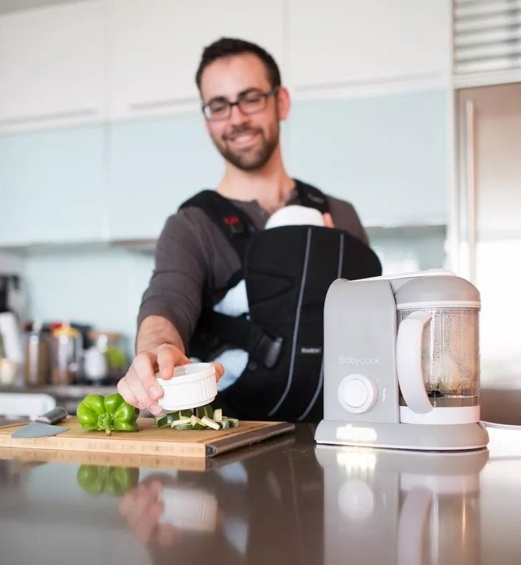 model cooking with infant in carrier, using a countertop baby food processor