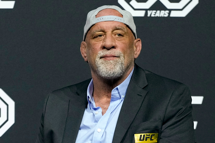 Man in a baseball cap and business attire sitting in front of a UFC backdrop