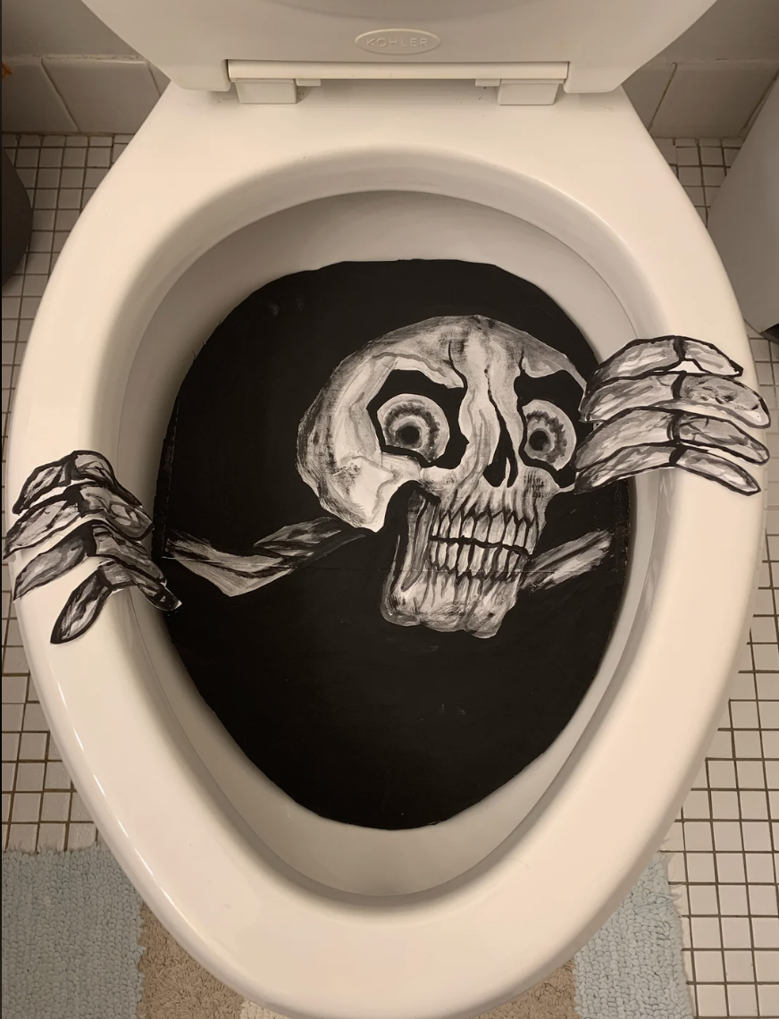 Toilet with a skull and hands decal, creating an illusion of a skeleton emerging from the bowl