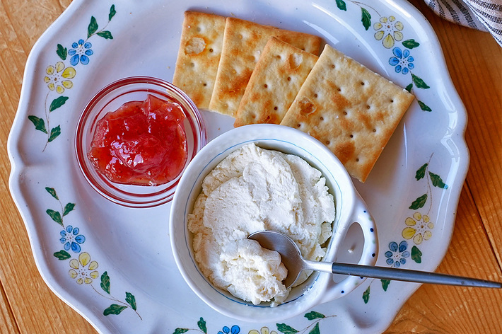 白い花柄の皿にクリームチーズとクラッカー、小さなジャムの入ったガラス容器が添えられています。