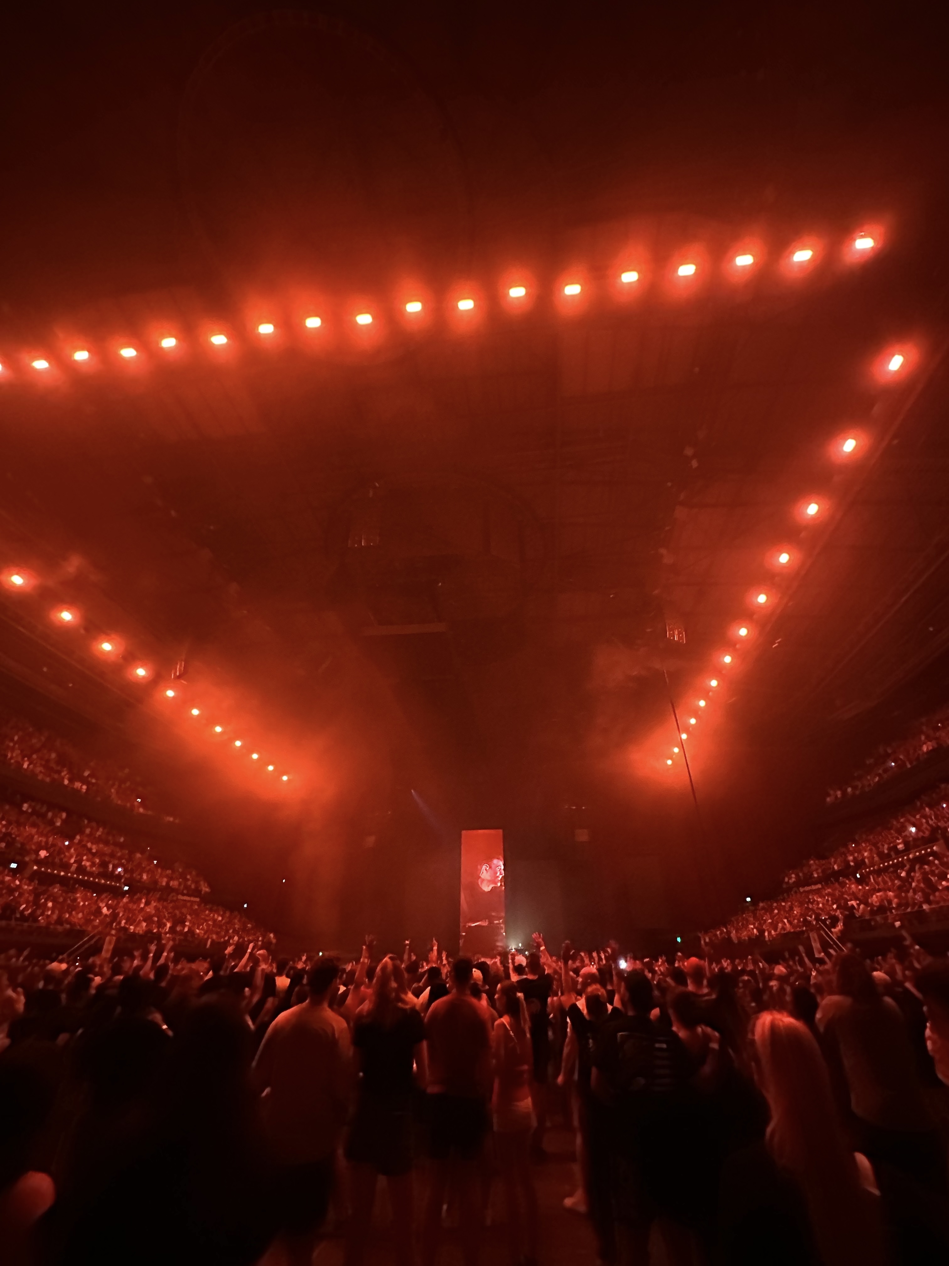 Crowd at a concert with stage lights overhead, creating a hazy atmosphere