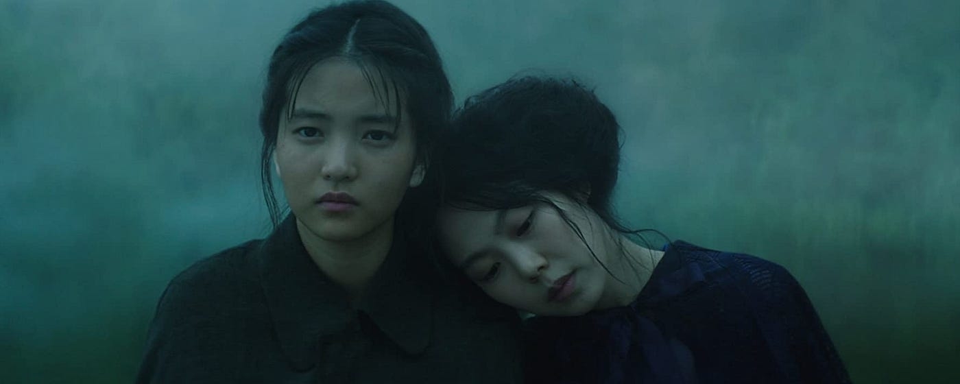 Two characters from a film, one resting her head on the other&#x27;s shoulder, with a somber expression