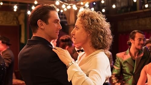 Two actors portraying characters in an intimate dance scene, with extras in the background