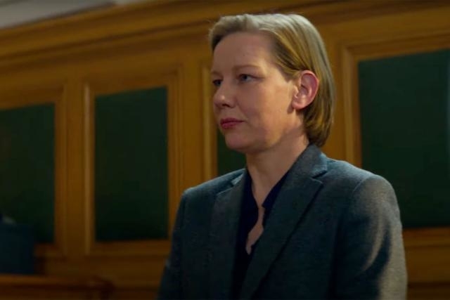 Woman in a courtroom setting, appearing stern, dressed in a professional suit