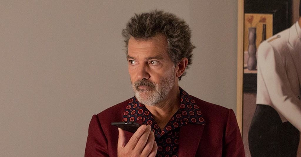 Antonio Banderas in a red patterned shirt, looking thoughtful, holding a phone to his ear