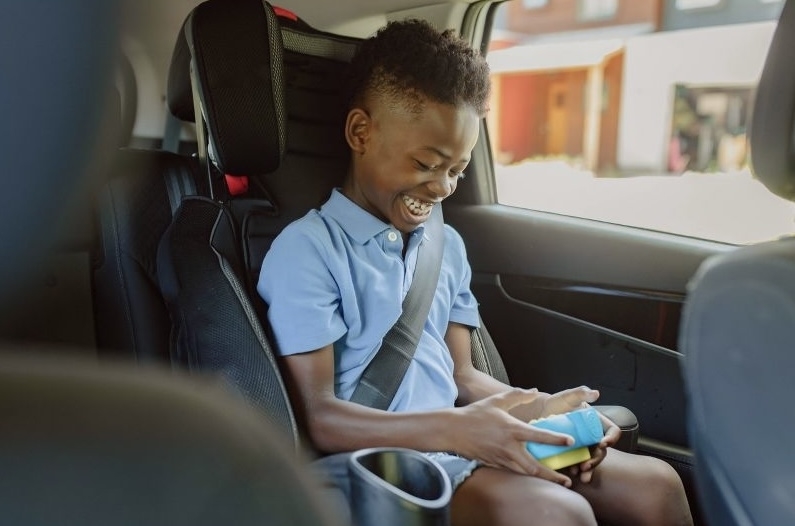 Child smiling while sitting in a car seat, playing with a smartphone