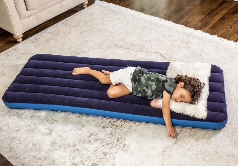 Child sleeping on a portable blue air mattress indoors