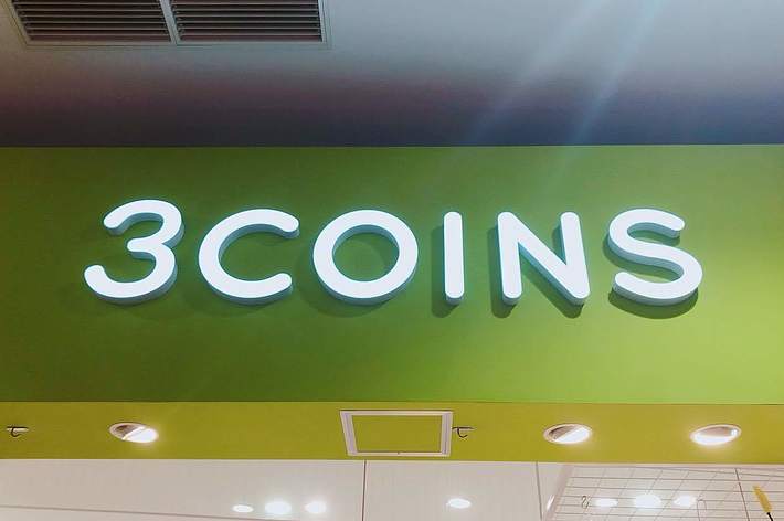 店舗のサイン「3COINS」が掲げられた壁、背景にショッピングモールの内装が見える。